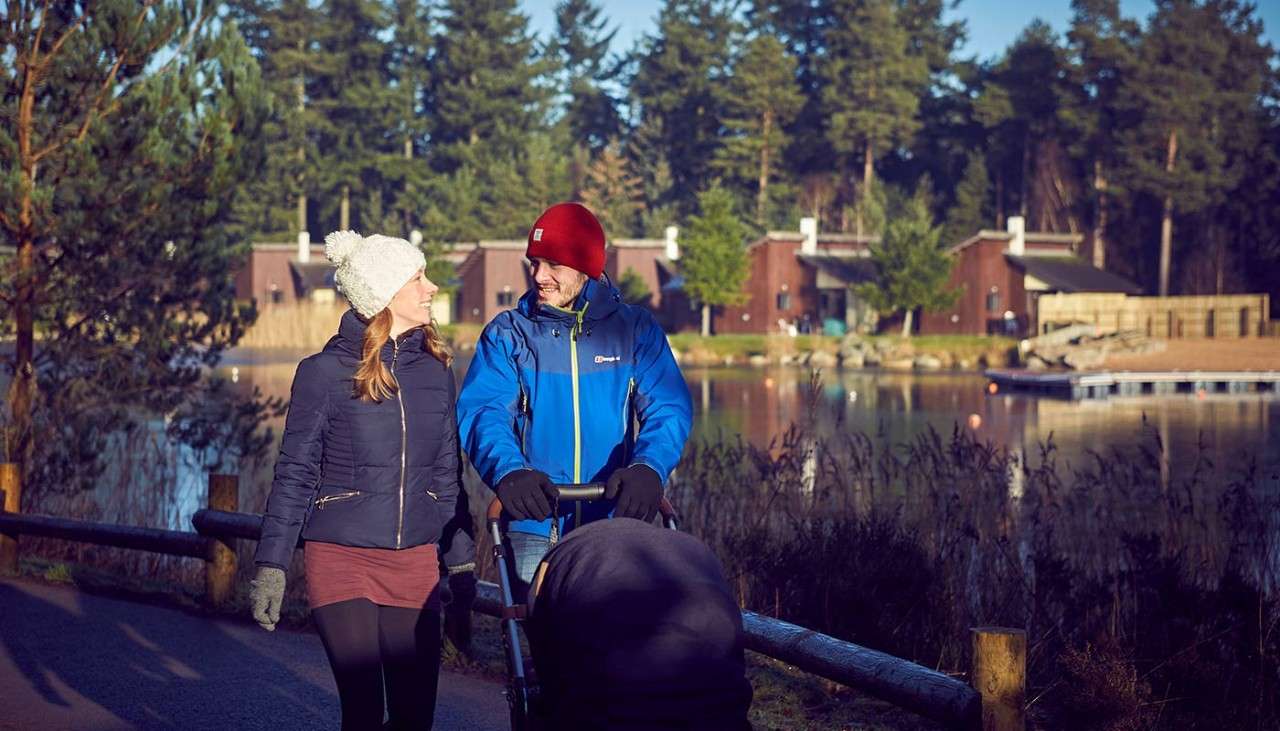 Couple pushing a pram past the lake wearing cosy hats and coats