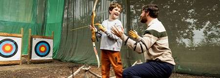 A father helping his son aim at a target with a bow and arrow.