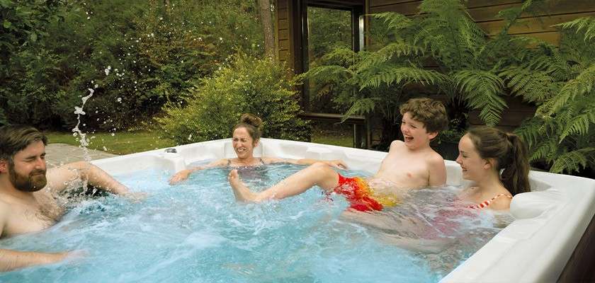 A family splashing around in a hot tub outside their lodge.