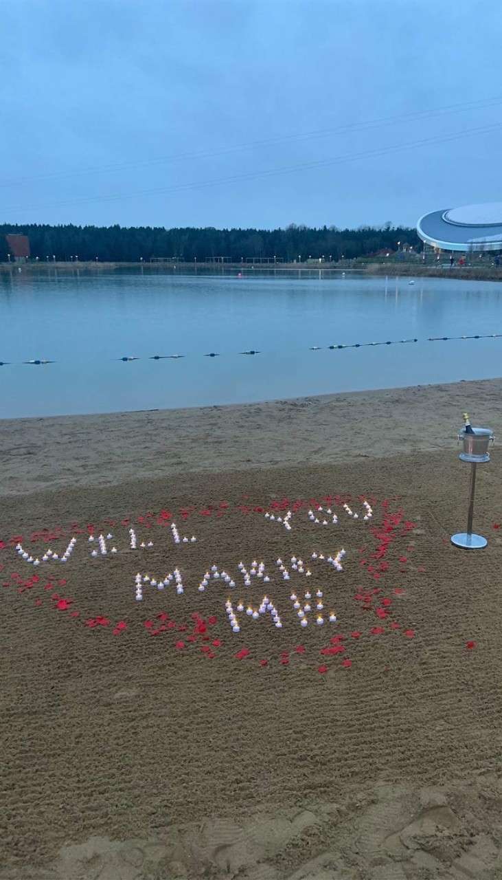 "Will you marry me" written on the beach with stones with a bottle of champagne in an ice bucket.