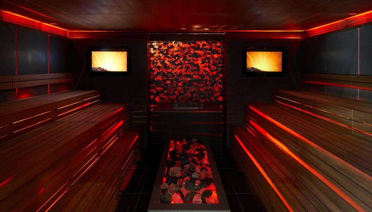 Lava Sauna illuminated in red with a coal themed glowing window display and stacked wooden benches.