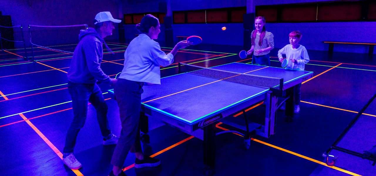 Family playing Table Tennis in a UV lit room